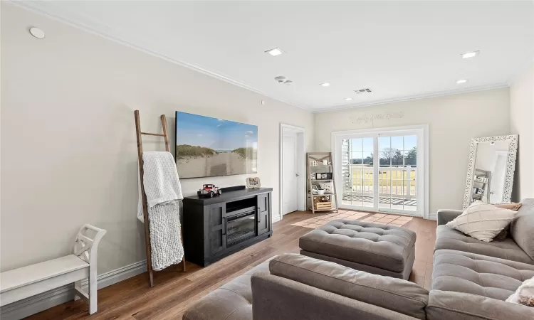 Living room with light wood-style flooring, baseboards, visible vents, and ornamental molding