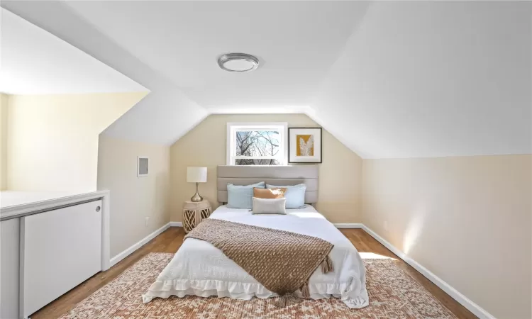 Bedroom with vaulted ceiling, wood finished floors, and baseboards