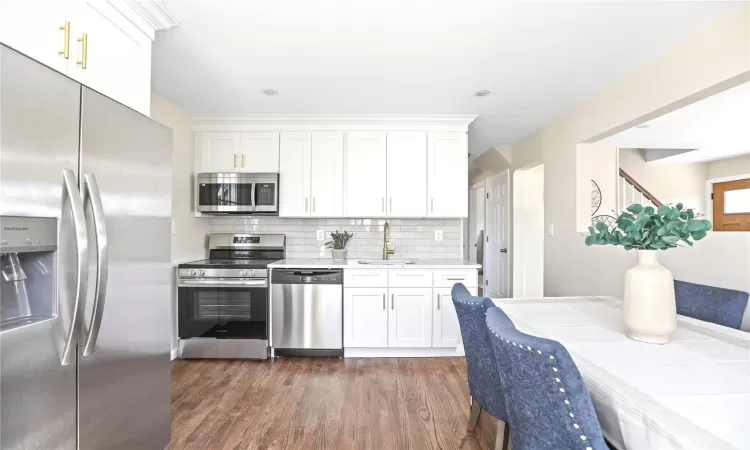 Kitchen featuring dark wood-style floors, a sink, stainless steel appliances, light countertops, and tasteful backsplash