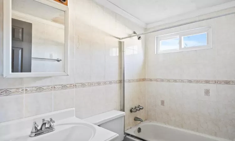 Full bathroom with tub / shower combination, crown molding, toilet, tile walls, and a sink