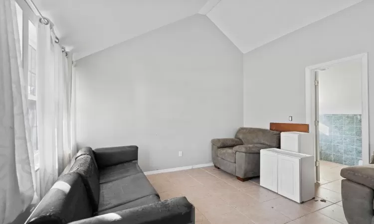 Living area featuring light tile patterned floors, baseboards, and lofted ceiling