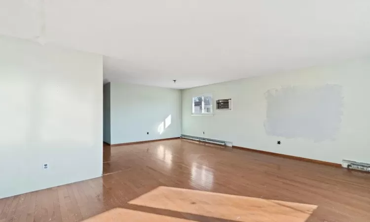 Empty room featuring baseboards, wood-type flooring, and a baseboard radiator