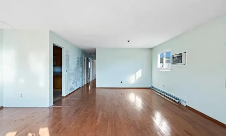 Spare room featuring baseboard heating, a wall mounted AC, baseboards, and wood-type flooring