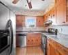 Kitchen with under cabinet range hood, appliances with stainless steel finishes, brown cabinetry, a ceiling fan, and a sink