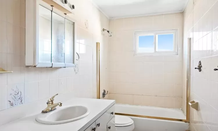 Bathroom with tasteful backsplash, tile walls, toilet, shower / tub combination, and vanity