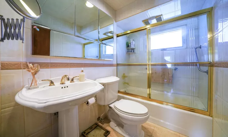 Full bathroom featuring toilet, tile walls, shower / bath combination with glass door, and tile patterned flooring