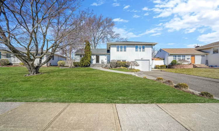 Split level home with aphalt driveway, board and batten siding, a front yard, and fence