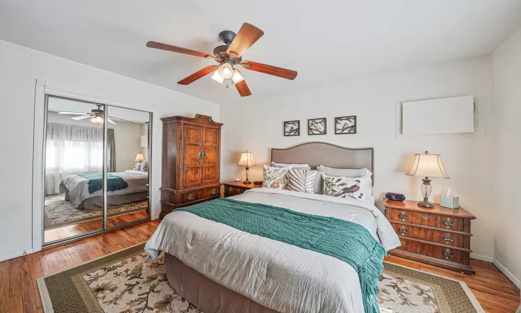 Bedroom featuring baseboards, ornamental molding, a closet, a ceiling fan, and wood-type flooring