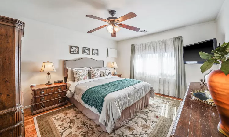 Bedroom with a ceiling fan, crown molding, wood finished floors, and visible vents