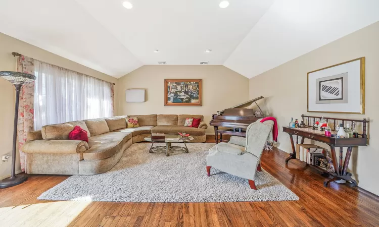 Living room featuring visible vents, wood finished floors, and vaulted ceiling