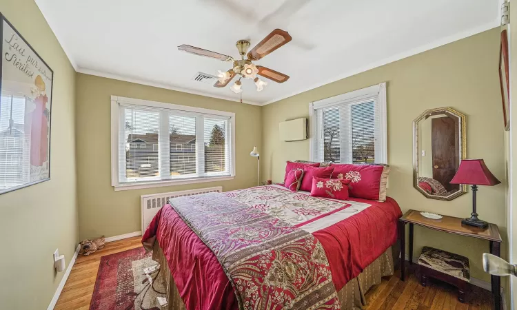 Bedroom featuring ornamental molding, radiator heating unit, baseboards, and wood finished floors