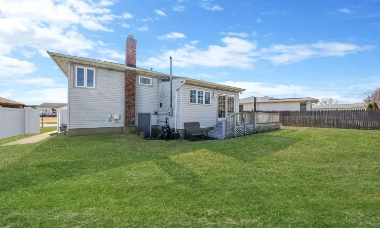 Rear view of house featuring a deck, a lawn, and a fenced backyard