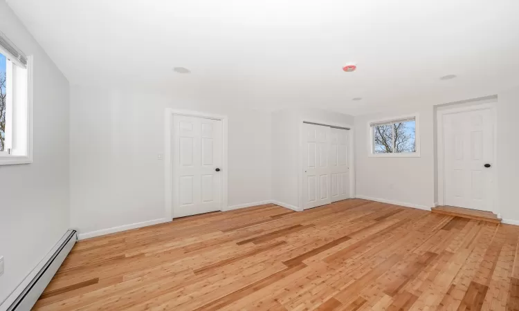 Unfurnished bedroom with light wood-type flooring, baseboards, baseboard heating, and a closet