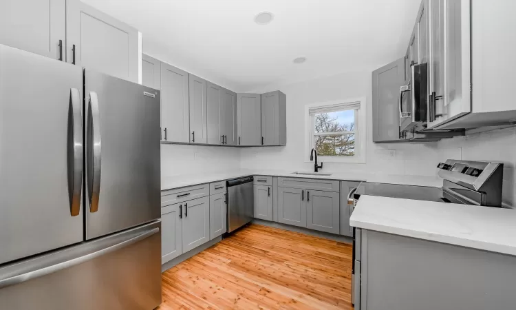 Kitchen featuring light stone countertops, gray cabinets, appliances with stainless steel finishes, and a sink