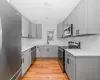 Kitchen featuring light wood finished floors, backsplash, gray cabinets, stainless steel appliances, and a sink