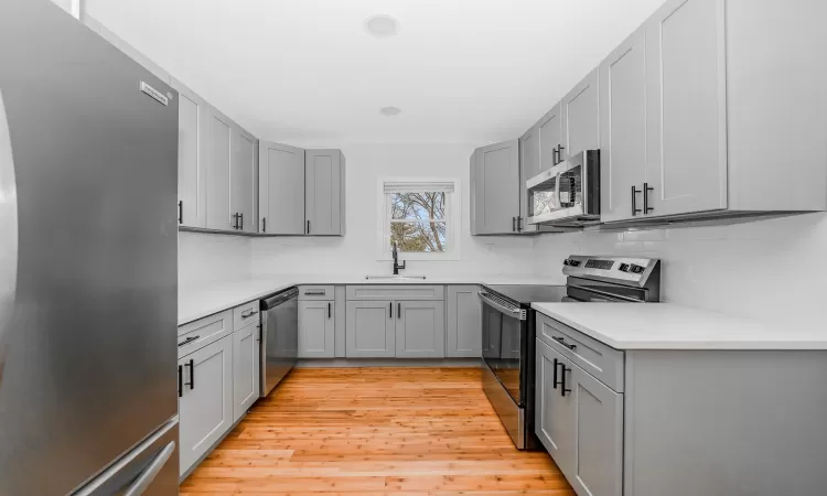 Kitchen featuring light wood finished floors, backsplash, gray cabinets, stainless steel appliances, and a sink