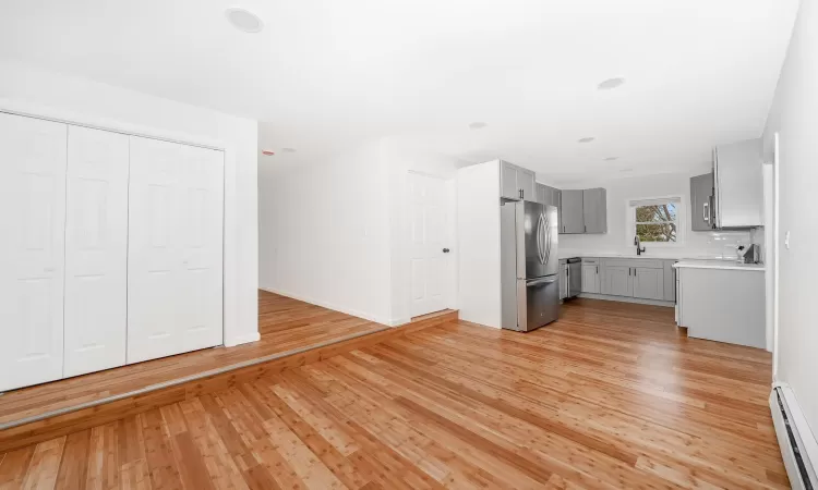 Kitchen with gray cabinetry, stainless steel appliances, light wood-style floors, light countertops, and baseboard heating