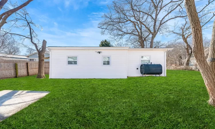 Back of property featuring heating fuel, fence, and a lawn