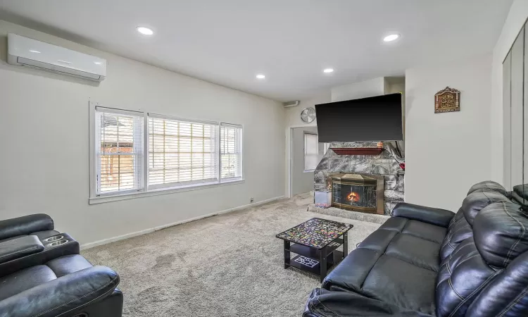 Carpeted living area with recessed lighting, a fireplace, a wall mounted AC, and baseboards