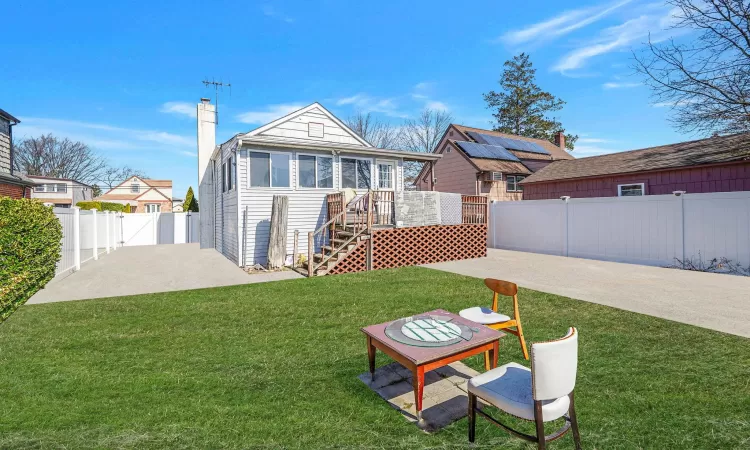 Back of property featuring a patio, a wooden deck, a fenced backyard, a chimney, and a lawn