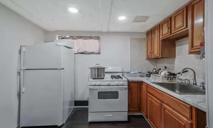 Kitchen featuring white appliances, brown cabinetry, a sink, light countertops, and tasteful backsplash