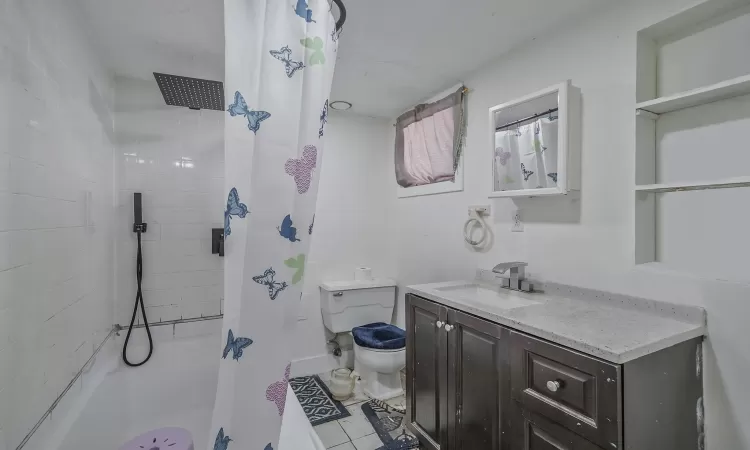 Bathroom with curtained shower, toilet, vanity, and tile patterned flooring