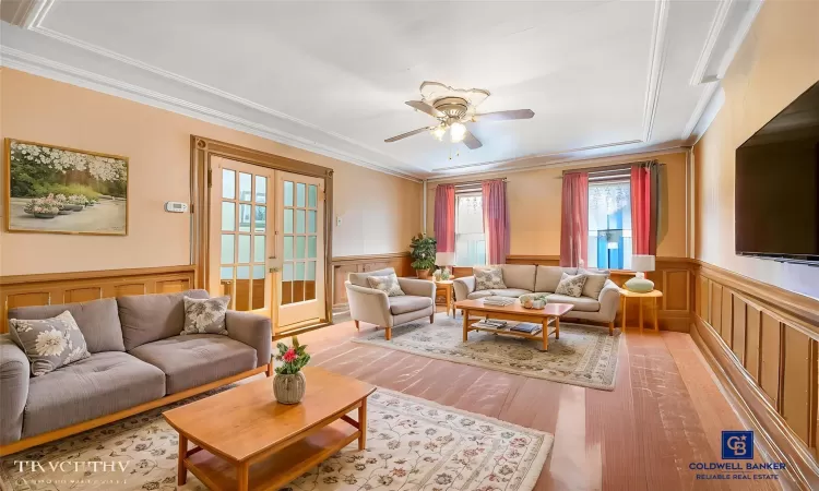 Living room featuring ceiling fan, french doors, wainscoting, crown molding, and light wood-type flooring