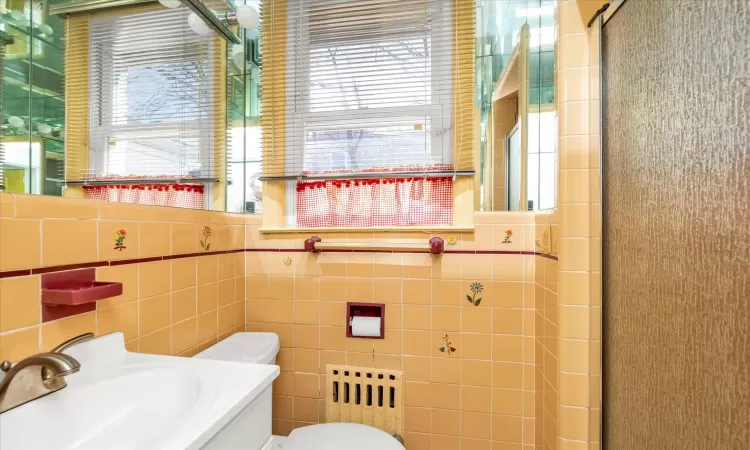 Bathroom with a sink, a shower with door, toilet, and tile walls