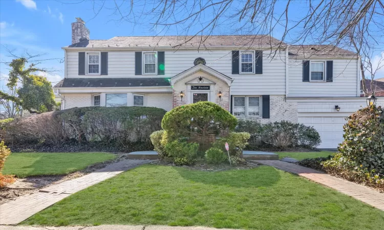 View of front of property with a front yard, an attached garage, brick siding, and a chimney