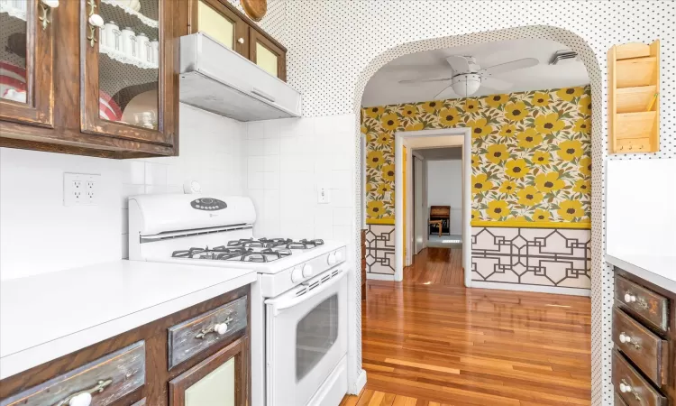 Kitchen featuring light wood finished floors, ventilation hood, ceiling fan, and gas range gas stove