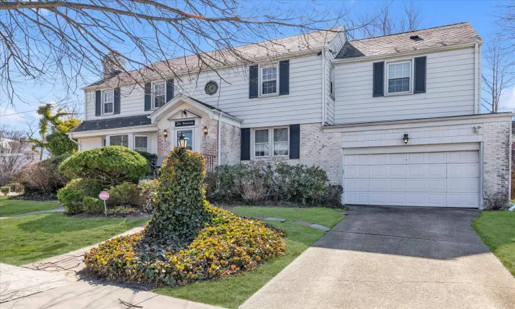 View of front of property featuring concrete driveway, a front yard, an attached garage, brick siding, and a chimney