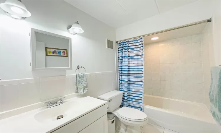 Full bath featuring visible vents, tile walls, toilet, shower / tub combo with curtain, and vanity