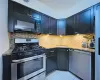 Kitchen with backsplash, light stone counters, dark cabinetry, stainless steel appliances, and a sink