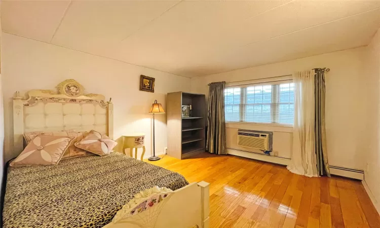 Unfurnished bedroom with baseboard heating, a wall mounted air conditioner, and wood-type flooring