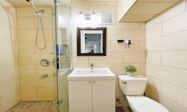 Bathroom with visible vents, toilet, a stall shower, tile walls, and vanity