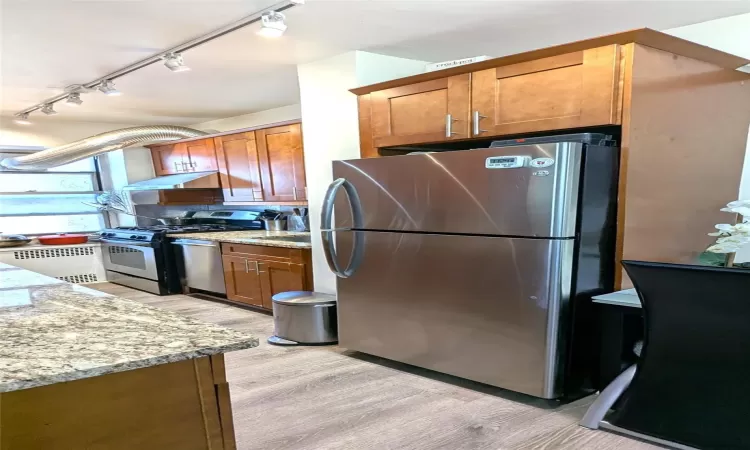 Kitchen featuring under cabinet range hood, light stone countertops, light wood-style floors, and appliances with stainless steel finishes