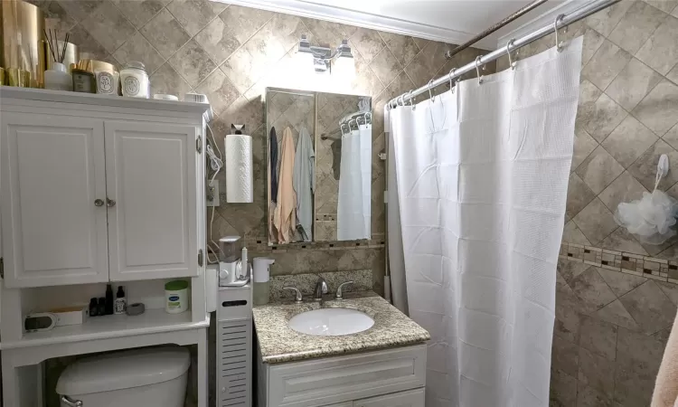 Bathroom with tasteful backsplash, tile walls, toilet, tiled shower, and vanity