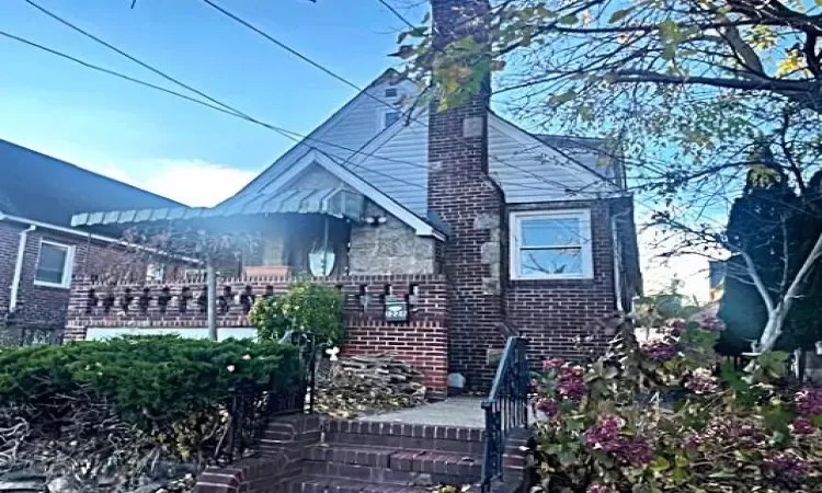 View of front of property featuring a fenced front yard, stone siding, covered porch, and a chimney