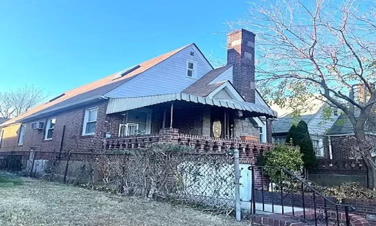 View of front of property featuring a fenced front yard, stone siding, covered porch, and a chimney