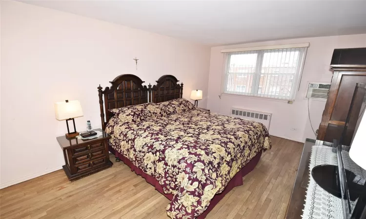 Bedroom with light wood-type flooring, baseboards, radiator, and an AC wall unit