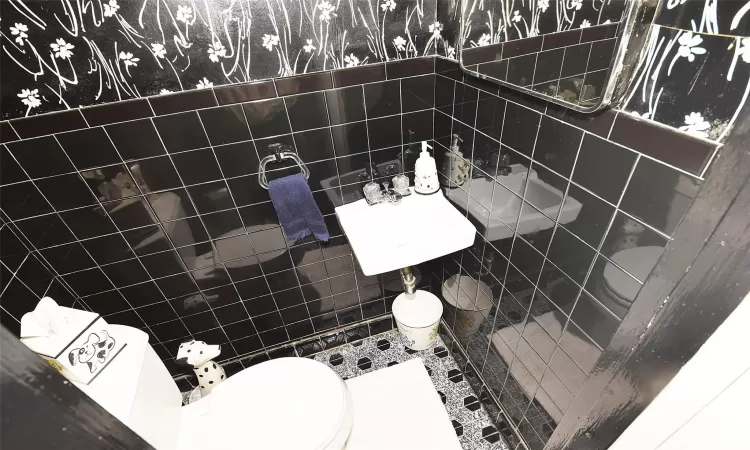 Half bath with toilet, tile walls, and a sink