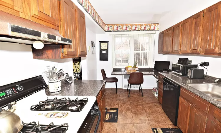 Kitchen featuring under cabinet range hood, a sink, gas stove, brown cabinetry, and dishwasher