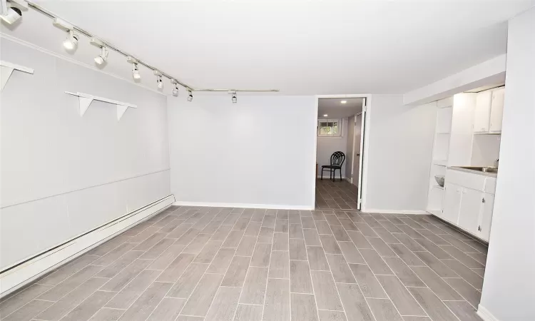 Empty room featuring wood tiled floor, rail lighting, baseboards, and a baseboard radiator