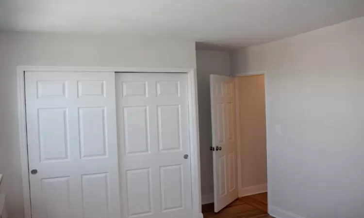 Unfurnished bedroom featuring dark wood finished floors, baseboards, and a closet