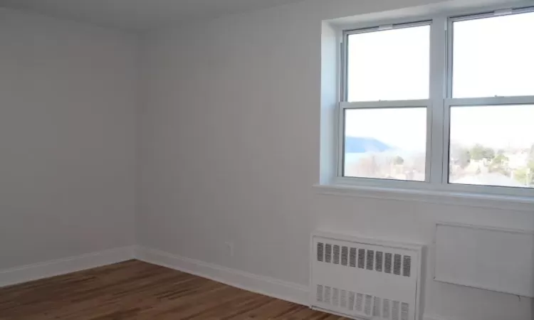 Unfurnished room featuring radiator heating unit, baseboards, and wood finished floors