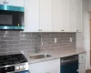 Kitchen with light stone counters, a sink, white cabinets, appliances with stainless steel finishes, and backsplash