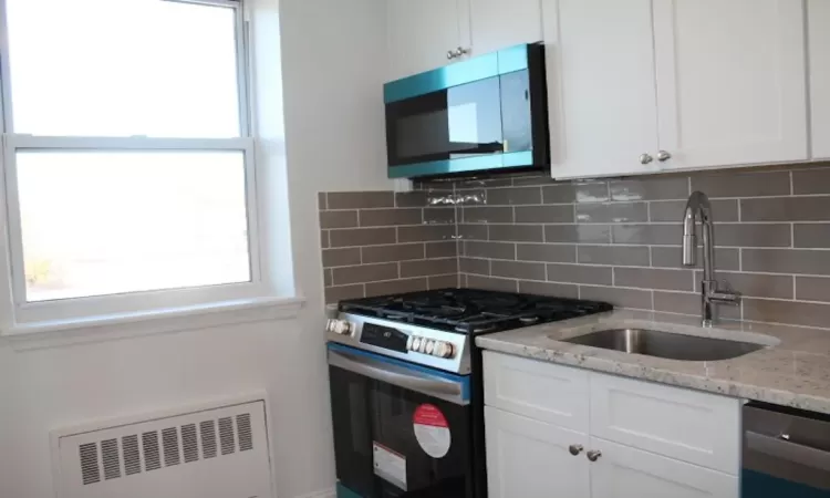 Kitchen featuring a sink, light stone counters, radiator heating unit, stainless steel appliances, and white cabinets