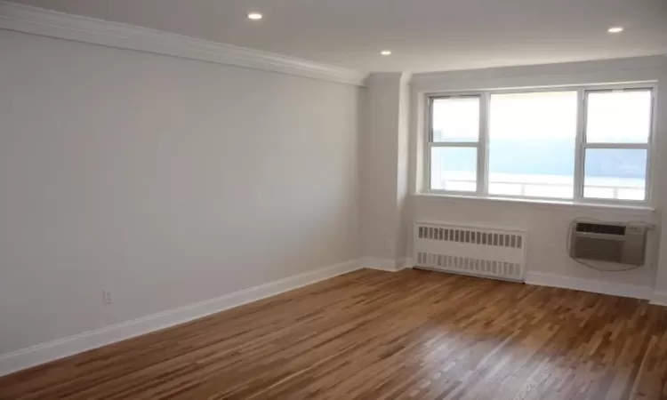 Empty room featuring crown molding, radiator heating unit, baseboards, and a wall mounted air conditioner