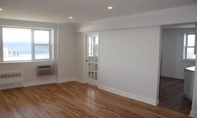 Empty room featuring wood finished floors, ornamental molding, radiator heating unit, and a wall unit AC