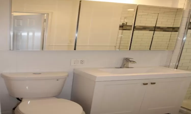 Full bathroom featuring tasteful backsplash, tile walls, toilet, a tile shower, and vanity